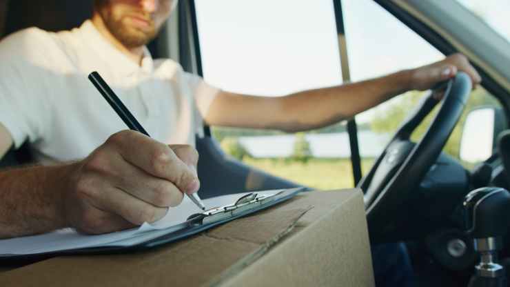 delivery driver in their van writing on a clipboard.
